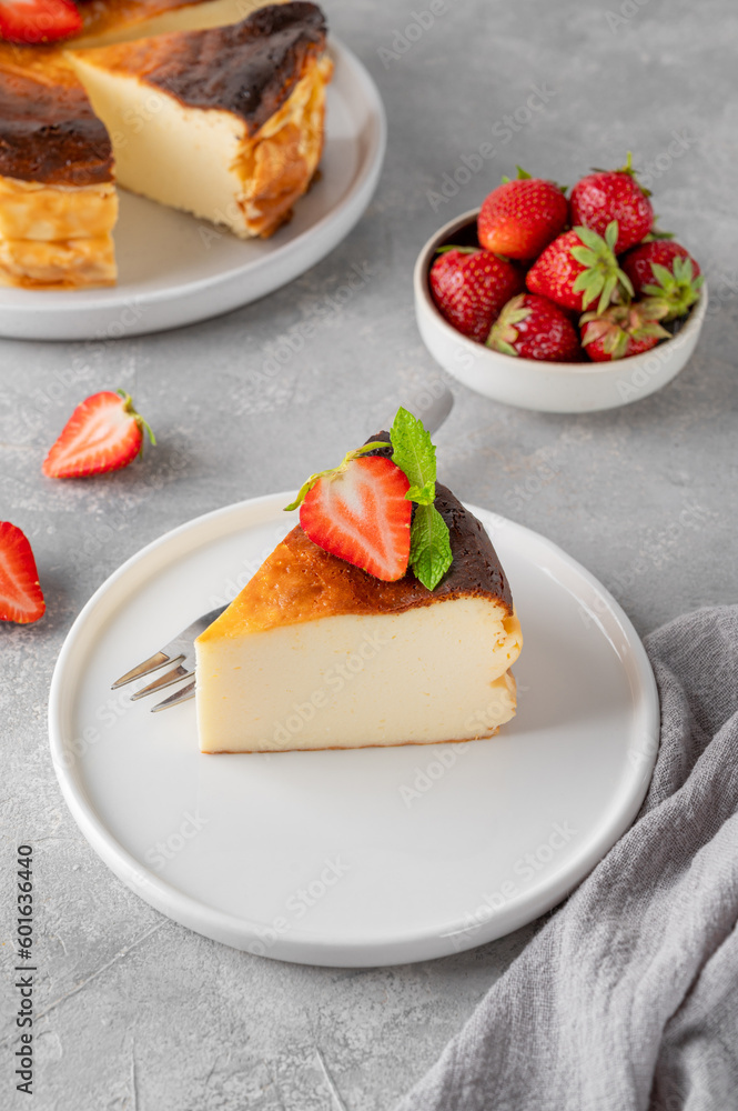 A piece of Basque burnt cheesecake or San Sebastian cheesecake with fresh strawberries on a white plate on a gray background. Selective focus. Copy space. A piece of Basque burnt cheesecake or San Sebastian cheesecake with fresh strawberries on a white plate on a gray background. Selective focus. Copy space.