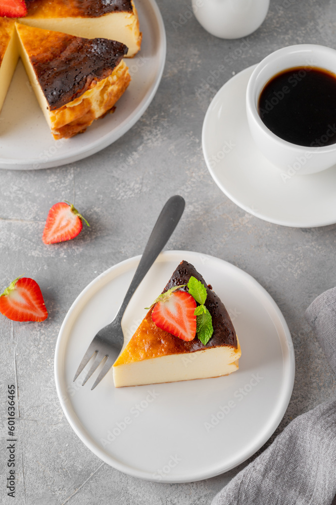 Fototapeta premium A piece of Basque burnt cheesecake or San Sebastian cheesecake with fresh strawberries on a white plate on a gray background. Selective focus. Copy space.