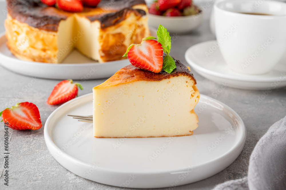 A piece of Basque burnt cheesecake or San Sebastian cheesecake with fresh strawberries on a white plate on a gray background. Selective focus. Copy space. A piece of Basque burnt cheesecake or San Sebastian cheesecake with fresh strawberries on a white plate on a gray background. Selective focus. Copy space.