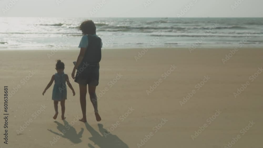 Mother films daughter with smartphone as she walks across beach to water at sunset Mother films daughter with smartphone as she walks across beach to water at sunset