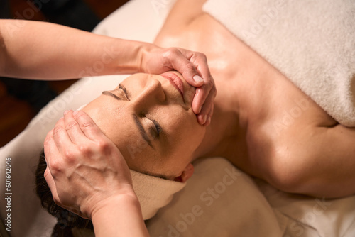 Experienced massotherapist giving facial massage to female client