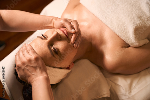 Qualified masseuse giving face and head massage to spa client