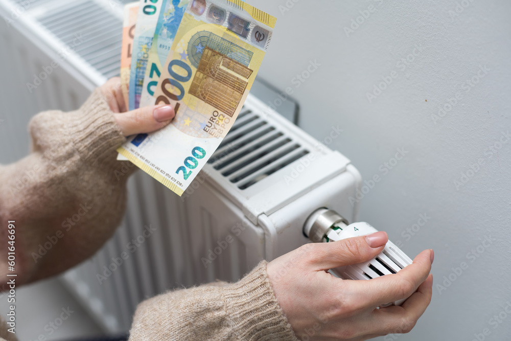 Woman holding cash in front of heating radiator. Payment for heating in winter