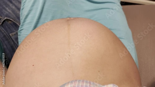 mom-to-be resting on couch, with exposed pregnant belly and baby kicking and moving, wearing a teal long skirt