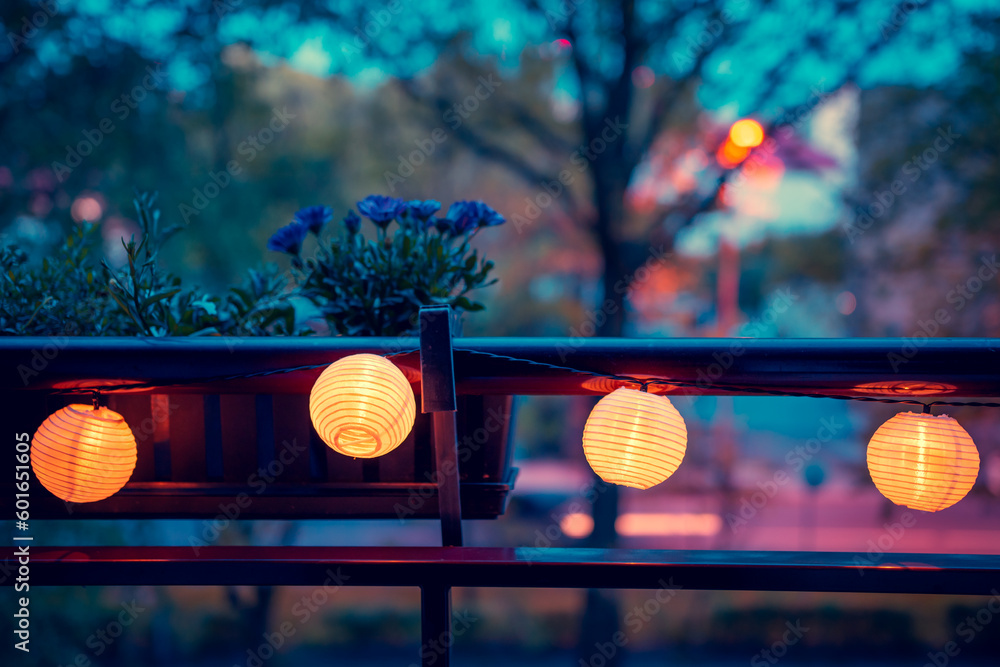 A lighted garland with solar lamps hung on the balustrade of the balcony. Mood light. African daisy in a balcony pot. Evening