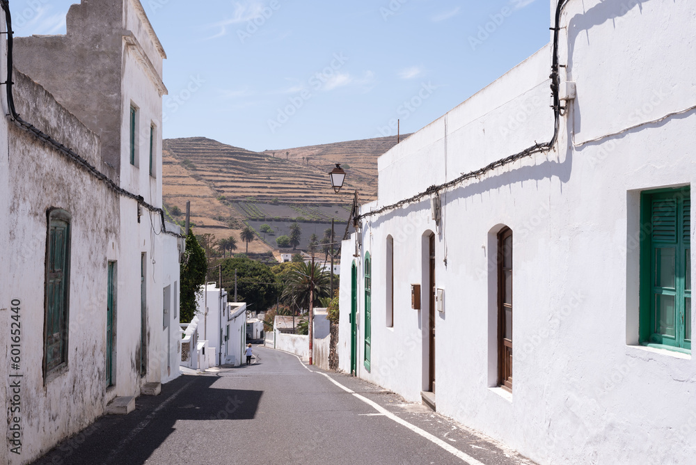 Street of small canarian village surrounded by white houses, palm trees and volcanic soil. Lanzarote, Canary Islands, Spain