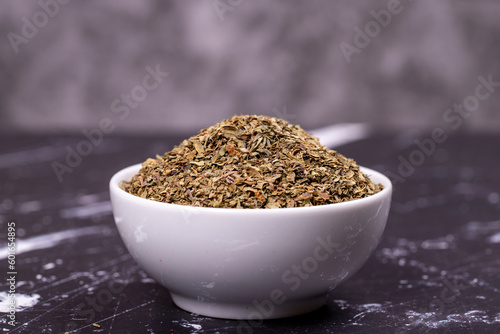Dried crushed basil on dark background. Dried ground basil powder spices in ceramic bowl. Spice concept