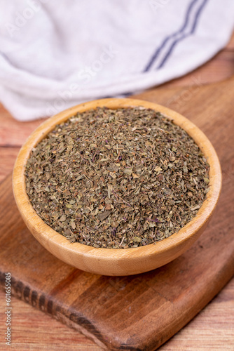 Dried crushed basil on wooden background. Dried ground basil powder spices in wooden bowl. Spice concept