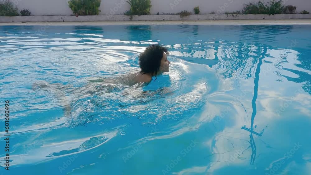 Curly hair hispanic multiracial woman swimming in luxury pool backlit by sunset sun, slow motion Curly hair hispanic multiracial woman swimming in luxury pool backlit by sunset sun, slow motion