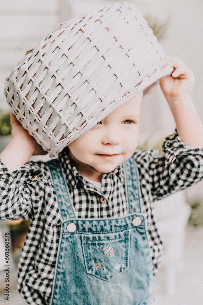 Little girl 1 years old with a basket on her head. Funny child plays puts a basket on her head like a hat and laughs, she is dressed in a plaid shirt and denim overalls. Funny moments with kids. Little girl 1 years old with a basket on her head. Funny child plays puts a basket on her head like a hat and laughs, she is dressed in a plaid shirt and denim overalls. Funny moments with kids.