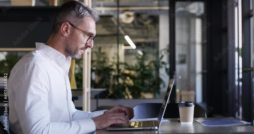 Laptop, documents and proposal with a business man working at a desk in his office for report or review. Computer, paperwork and typing an email with a male employee at work on a company project