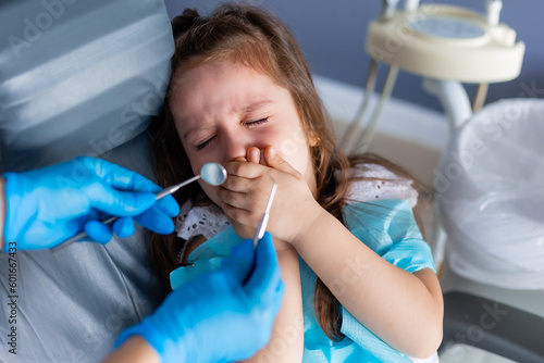 little brunette girl at the reception is crying, afraid. Pediatric dentistry