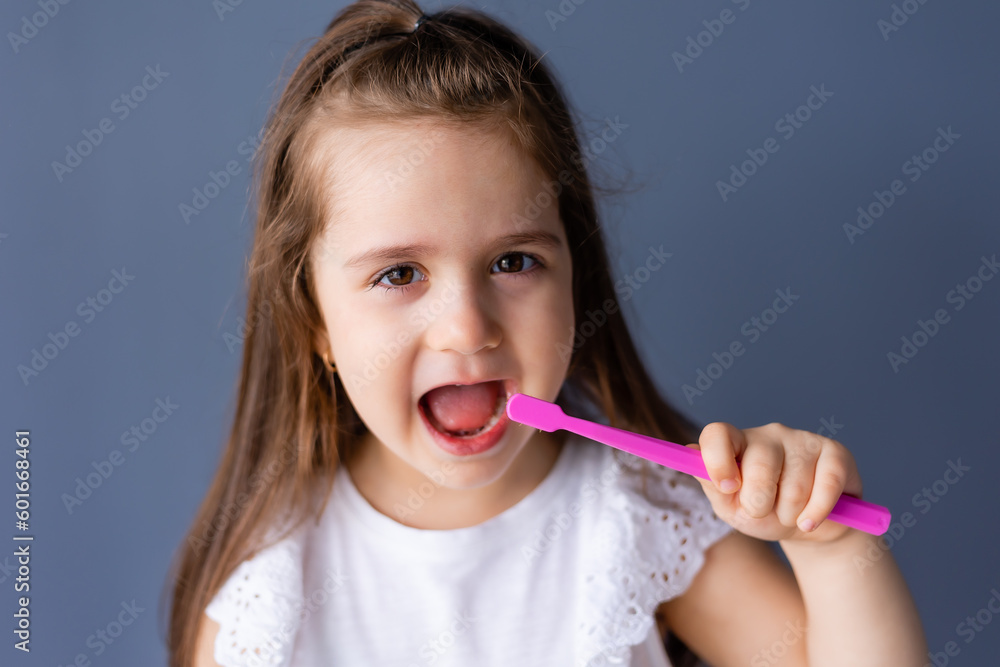 a little brunette girl holds a toothbrush in her hands on a plain gray background, space for text. Pediatric dentistry a little brunette girl holds a toothbrush in her hands on a plain gray background, space for text. Pediatric dentistry