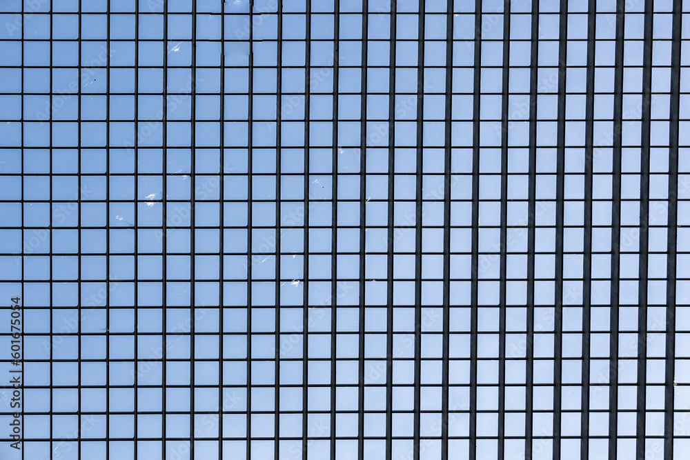 Open metal grid on roof of a tunnel against blue sky, metal structure with grid lattice with small dust particles, sunlight passing between the openings on a sunny day Open metal grid on roof of a tunnel against blue sky, metal structure with grid lattice with small dust particles, sunlight passing between the openings on a sunny day