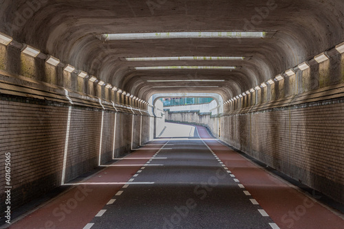 Front view of interior of an empty vehicular tunnel with cycle lanes with a curve in background, brick walls, concrete roof and openings where sunlight enters, Susteren, South Limburg, Netherlands
