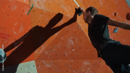 A professional athlete climber performs a difficult jump by grabbing a climbing wall with his hand during indoor training. A millennial man in dark sportswear on a climbing wall. High quality 4k