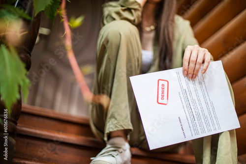 Young brunette long hair girl cries hysterically after being denied a mortgage loan. Depressive sad eviction female millenial holding rejection document copy space banner photo