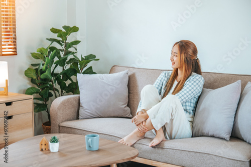 Pensive relaxed Asian woman relax and drinking coffee on sofa at home