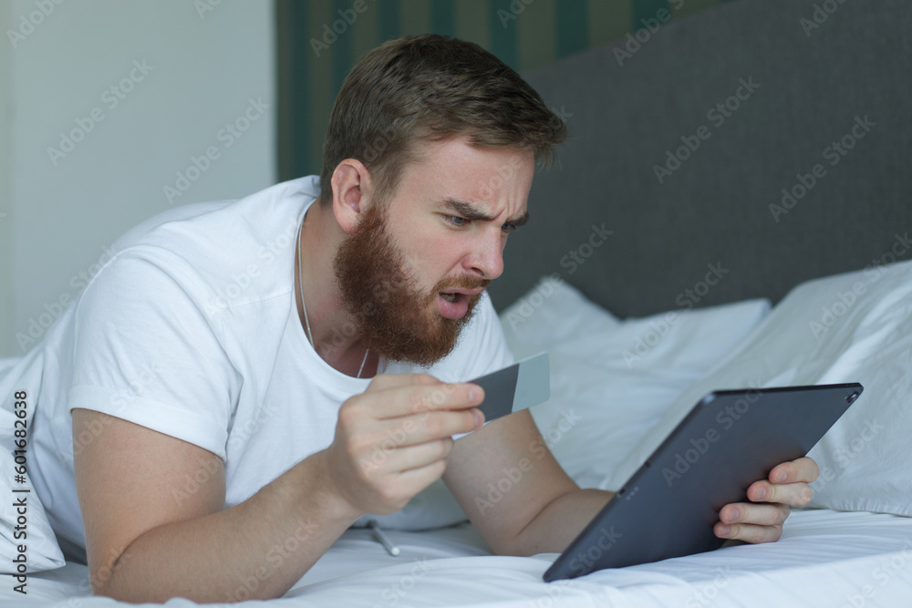 Naklejka premium Nervous sad upset confused young man, stressed worried guy having problem with paying, buying online, payments with credit blocked bank card, looking at screen, monitor of laptop. Internet fraud