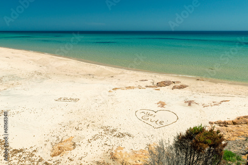 Paradise beach with heart shape drawn in the sand and text "Alles gutte" in German language, turquoise sea and blue sky. Santa Margherita di Pula beach, Sardinia, Italy, Mediterranean sea.