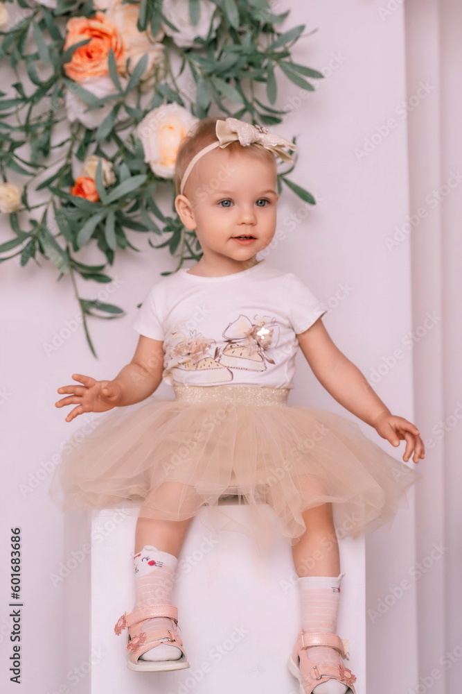 Baby girl elegant dress. A one-year-old girl in a puffy skirt and a white T-shirt poses against the backdrop of a bright room.