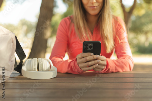 Blonde young girl in sportswear is in the park chatting on the mobile.