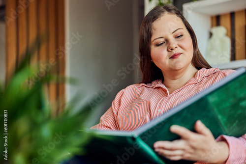 A pretty curvy woman enjoying while looking at her family photo album, at home. photo