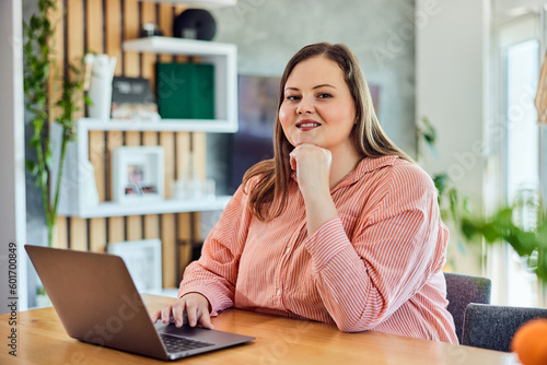 Portrait of a smiling plus-size woman, working over the laptop at home.