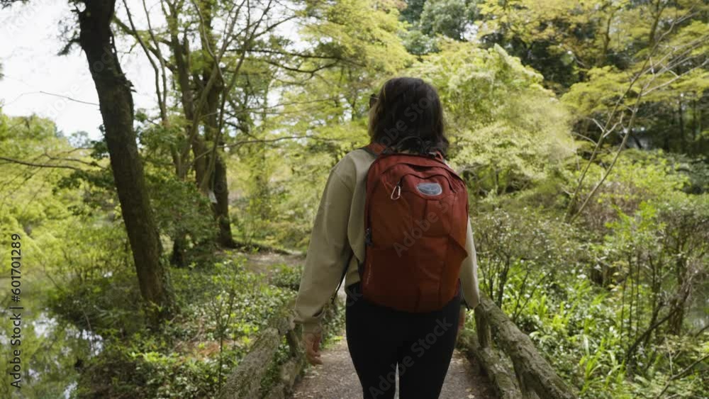 Slow motion tracking shot of a female hiker walking across a small bridge in a forest Slow motion tracking shot of a female hiker walking across a small bridge in a forest