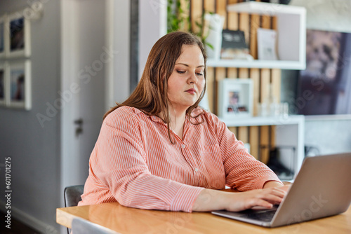 A curvy businesswoman working and typing on a laptop at her home office.