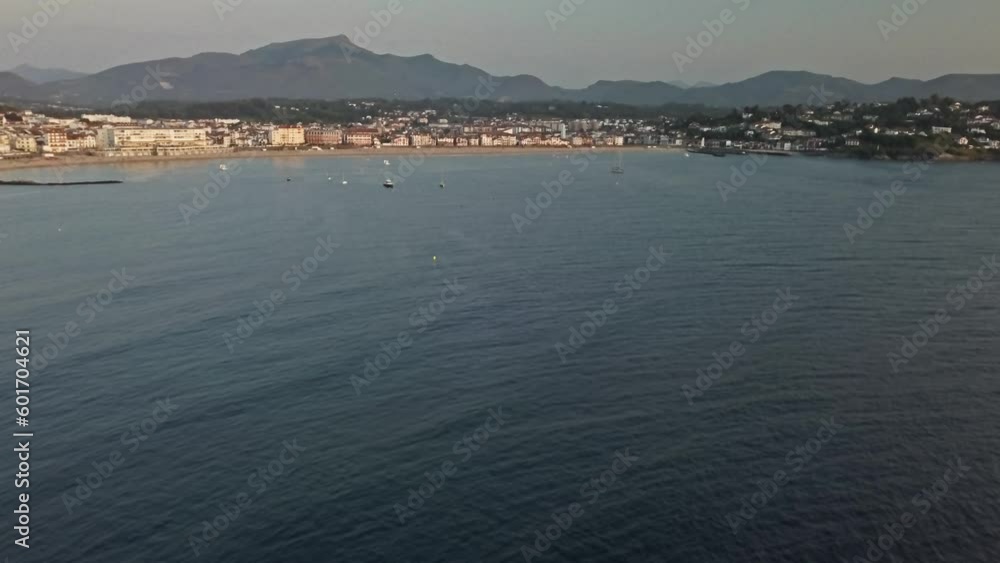 Rising aerial dolly showcases cute harbor town and coastline with jagged mountain ridgeline behind Rising aerial dolly showcases cute harbor town and coastline with jagged mountain ridgeline behind