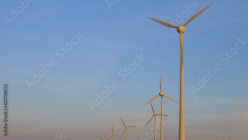 Beautiful view of wind turbines generating renewable energy in the wind farm, green countryside landscape, vibrant sunny spring evening with golden hour light, distant medium wide shot photo