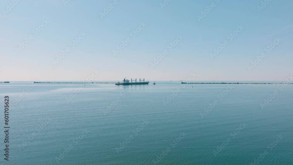 Aerial establishing view of large cargo ship leaving Port of Liepaja (Latvia), sunny spring day, calm Baltic sea, distant wide drone shot moving forward Aerial establishing view of large cargo ship leaving Port of Liepaja (Latvia), sunny spring day, calm Baltic sea, distant wide drone shot moving forward