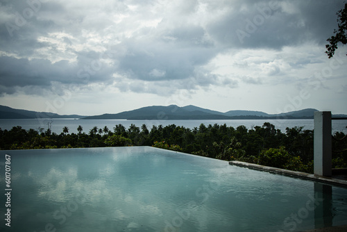 Wide angle view of a beautiful infinity pool in a tropical island overlooking the sea and other islands of exotic archipelago. Overcast day  almost sunset  water reflections.
