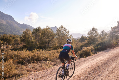 Fit female cyclist riding a gravel bicycle on the road in hills with mountain view, Alicante region in Spain 