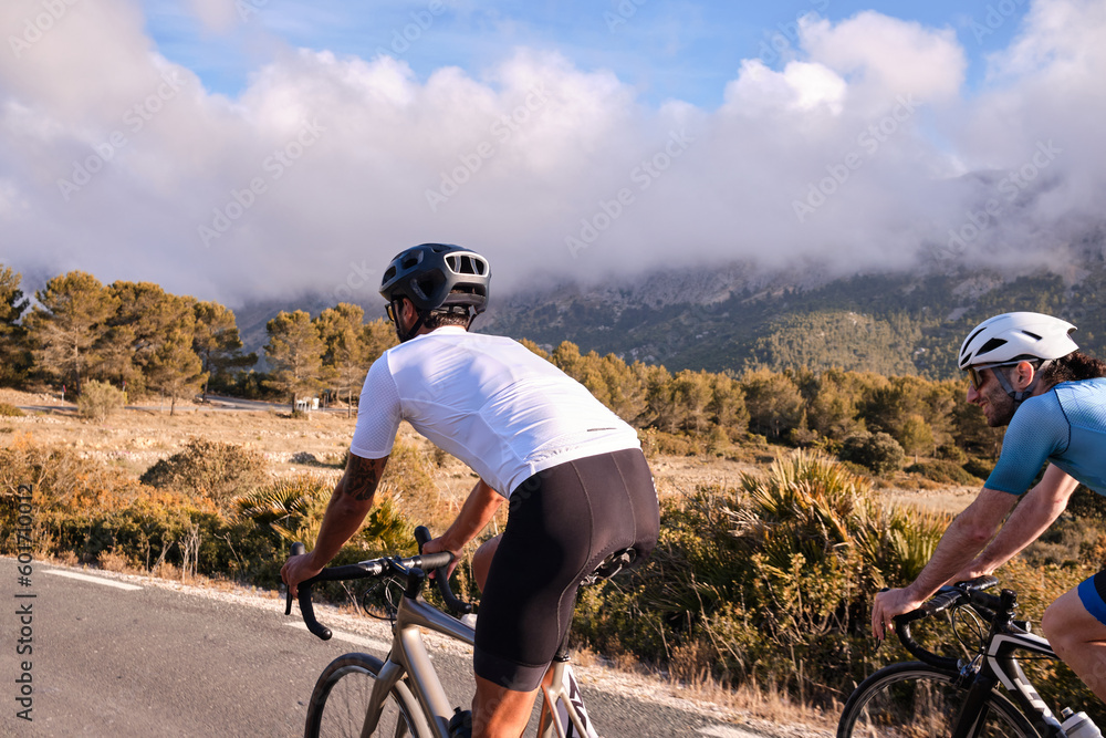 Fototapeta premium Cyclists in full cycling gear and helmets ride their road bikes on mountain road at sunset. Sportsmen training hard on bicycle outdoors. Spain