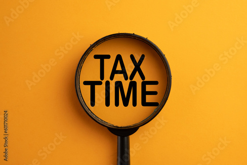 View through a magnifying glass on TAX TIME word over orange background use for tax,Financial,Business,Accounting concept.