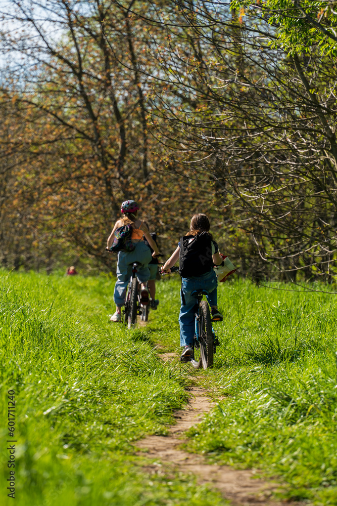 Group of children riding their bikes on a dirt trail on a sunny spring day among green grass, bike ride, children cycling in the woods, healthy lifestyle, authentic sustainability