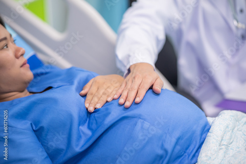 Man male obstetrician doctor in white uniform coat gown with stethoscope to check womb stomach in delivery room. gynecologist in gown coat sit and hand touch check womb pregnant abdomen mother.