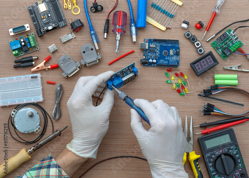 An engineer's hands are assembling a breadboard from an Arduino microcontroller, surrounded by electronics tuning tools. View of the electronic laboratory bench with peripherals and expansion boards. photo