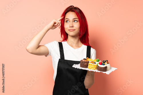 Pastry chef holding a muffins isolated on pink background having doubts and thinking