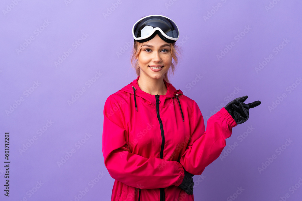 Skier teenager girl with snowboarding glasses over isolated purple background pointing finger to the side Skier teenager girl with snowboarding glasses over isolated purple background pointing finger to the side