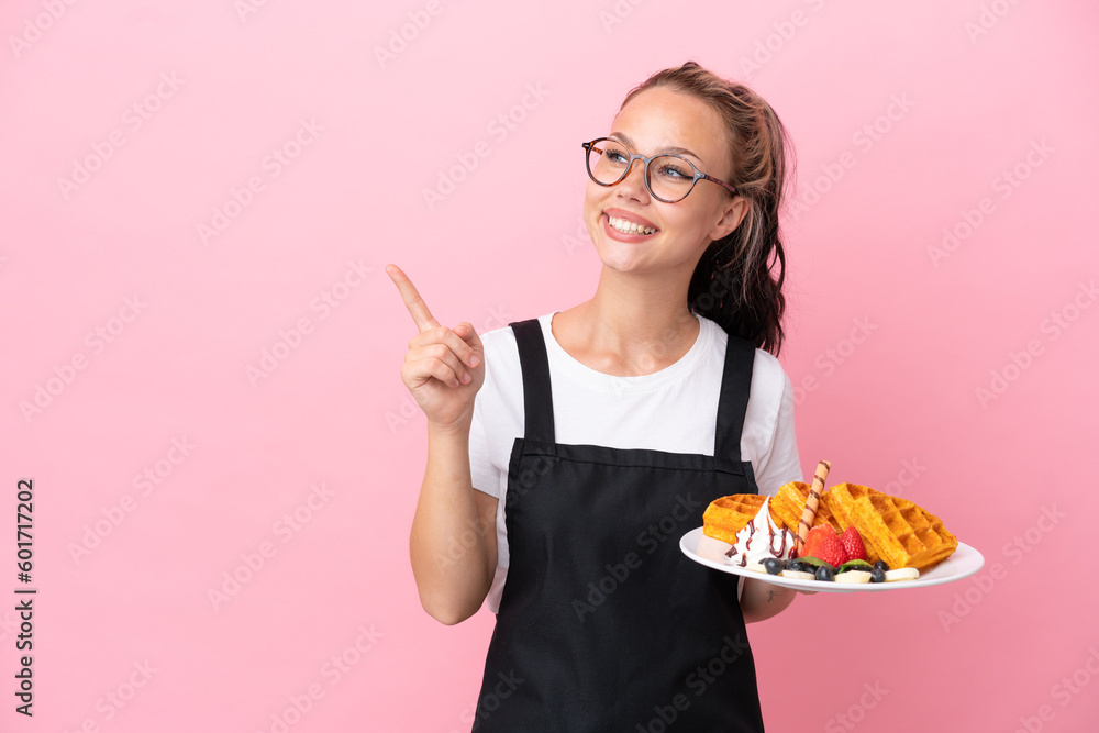 Restaurant waiter Russian girl holding waffles isolated on pink background intending to realizes the solution while lifting a finger up Restaurant waiter Russian girl holding waffles isolated on pink background intending to realizes the solution while lifting a finger up