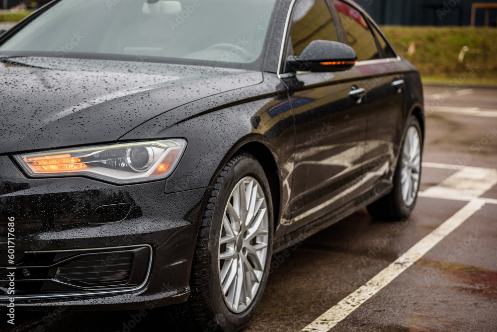 Front left headlight on a modern black car. Black metallic bumper car with light and car wheel. Car lamp signals for turning a car on street. Exterior automobile closeup. Side view of modern new car.