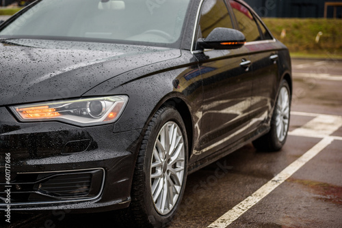 Front left headlight on a modern black car. Black metallic bumper car with light and car wheel. Car lamp signals for turning a car on street. Exterior automobile closeup. Side view of modern new car.