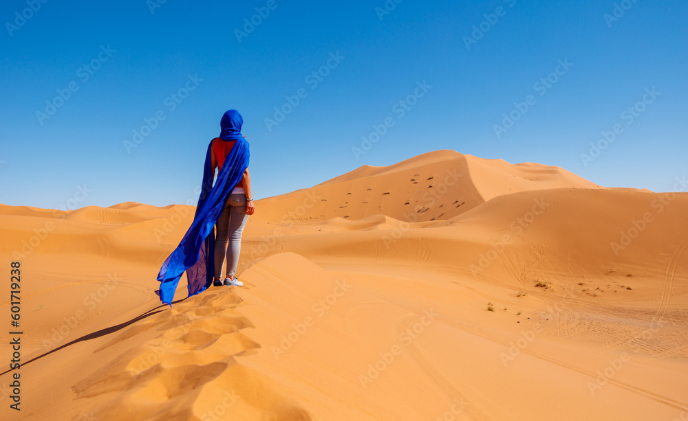 Rear view of woman wearing waving blue turban in the desert- Sahara desert in Morocco