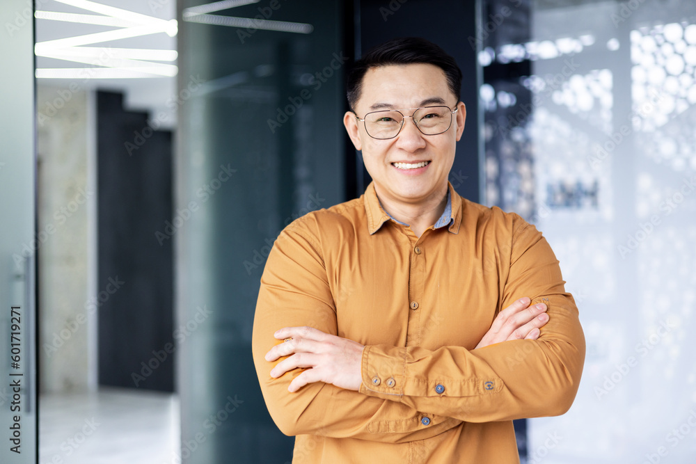 Obraz premium Portrait of successful asian businessman, man inside office wearing shirt and glasses smiling and looking at camera, investor broker with crossed arms near window.