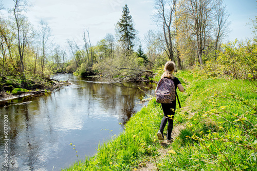 Back view of 9 year old girl hiking, walking alone in the forest by the river with a backpack in early spring. Beautiful idyllic nature.