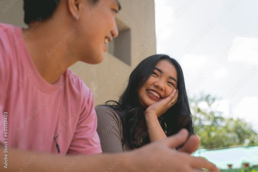 A guy wearing a pink shirt leaning on a rail in front of a building while smiling at the lady beside him is a lady who's resting her chin on her hand and widely smiling at the guy . A guy wearing a pink shirt leaning on a rail in front of a building while smiling at the lady beside him is a lady who's resting her chin on her hand and widely smiling at the guy .