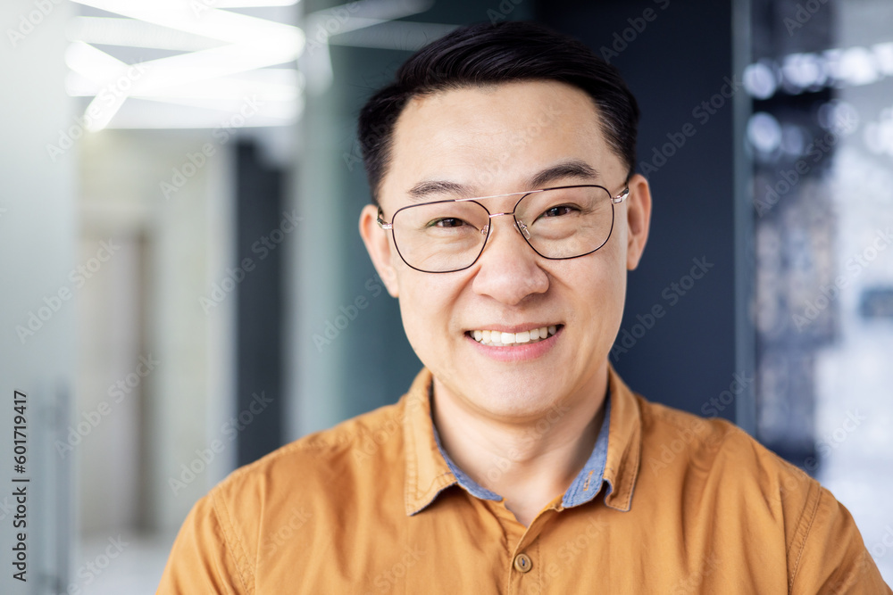 Close up photo portrait of successful young Asian investor, man in glasses smiling and looking at camera in shirt, businessman working inside modern office building, satisfied accountant financier. Close up photo portrait of successful young Asian investor, man in glasses smiling and looking at camera in shirt, businessman working inside modern office building, satisfied accountant financier.
